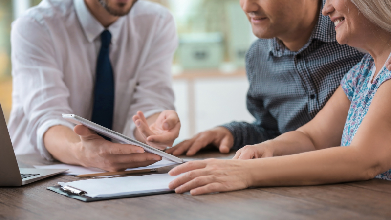 An image of an insurance agent displaying options to an elderly couple, with a tablet.