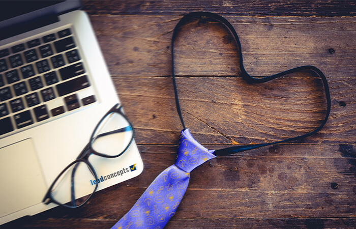 Image of half of a laptop, a pair of glasses, and a tie in the shape of a heart, with Lead Concepts iconography on the tie.